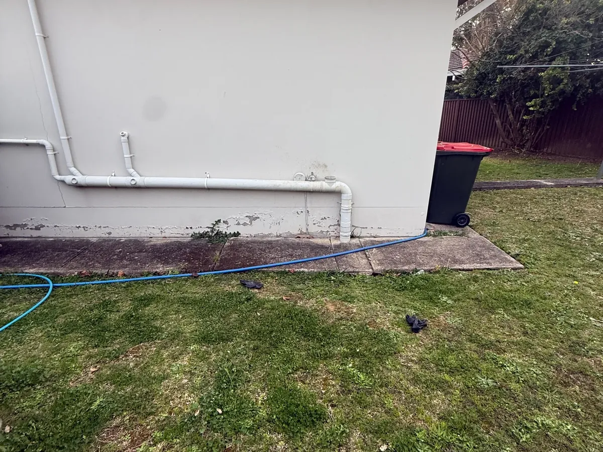 Blue jet hose laid across the lawn beside the waste pipes of a house in Toongabbie