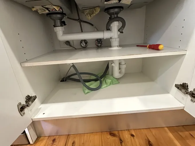 Sink wastes, water valves and a dishwasher hose under a double sink mid-swap in Woolloomooloo