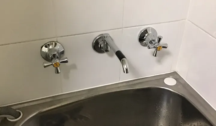 Wall-mounted laundry taps and spout above a stainless steel laundry tub