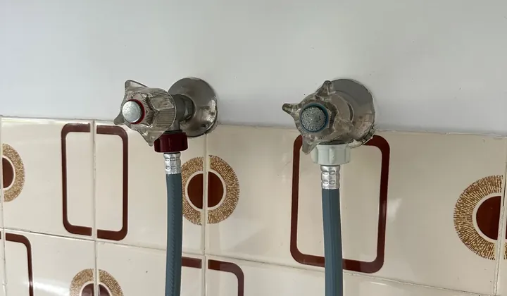 Washing machine taps with hot and cold inlet hoses on a tiled laundry wall