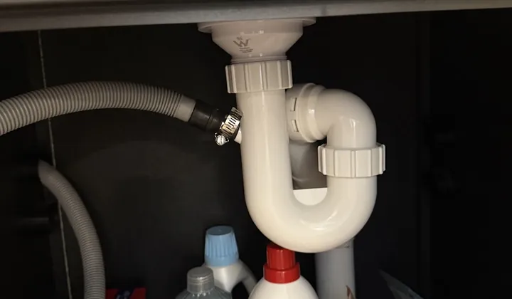 Washing machine waste hose clamped to a trap under a laundry sink