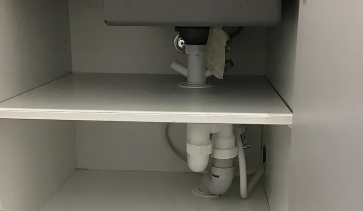 Open sink cabinet showing the waste pipes and trap underneath