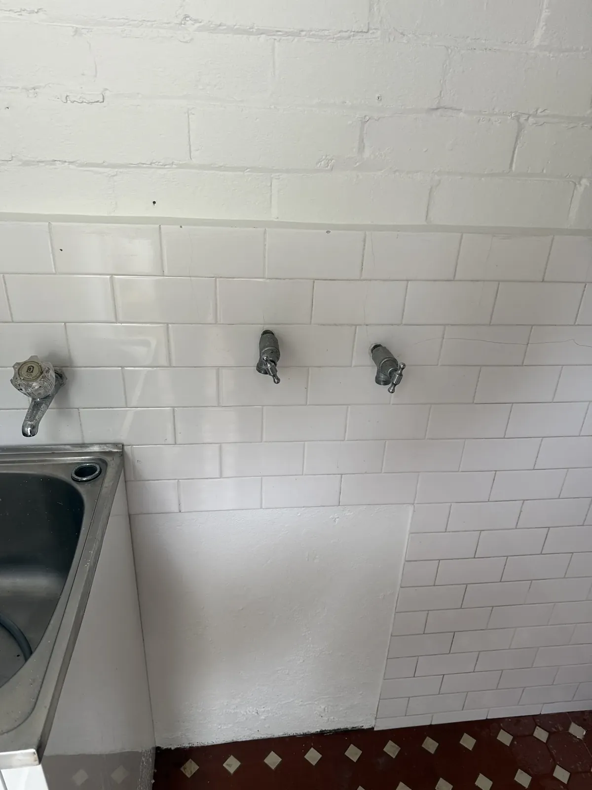 Laundry wall with washing machine taps and a stainless tub tap above a stainless laundry tub