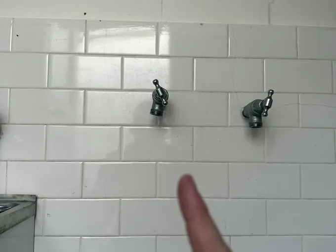 Washing machine taps on a white tiled laundry wall being pointed out