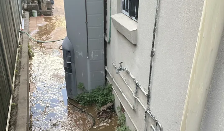 Muddy water flooding the side path of a house, past the hot water system, in Earlwood