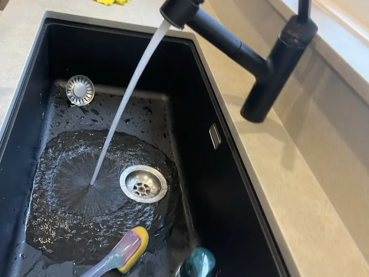 Dirty water sitting in a kitchen sink with the tap running in Artarmon
