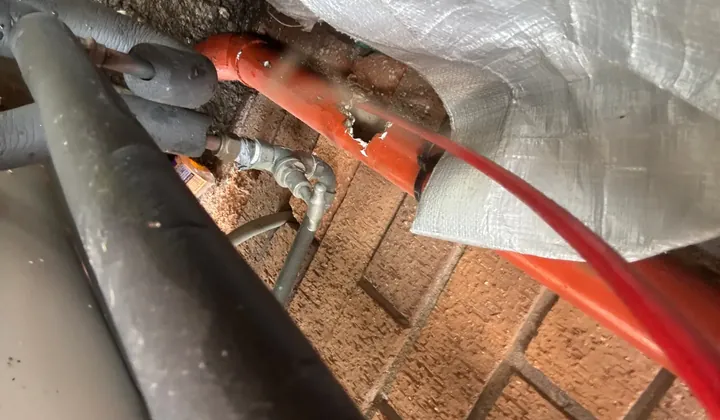 Orange drain pipe with a broken hole in its side under a Wakeley home