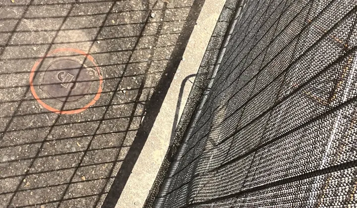 Sewer access cover marked with an orange circle on a concrete path