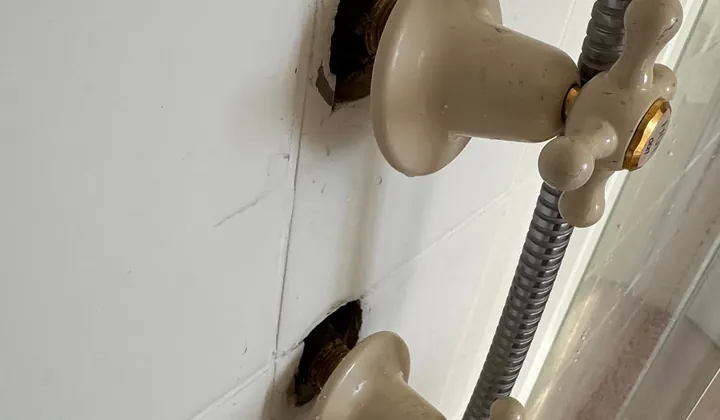 Shower taps with their cover plates off, showing the holes in the tiles around the tap bodies in Prestons