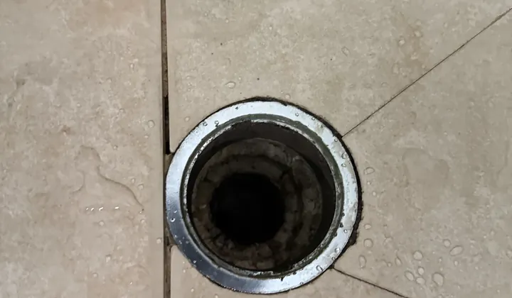 Close view of a bathroom floor drain with cracked grout lines around it in Granville
