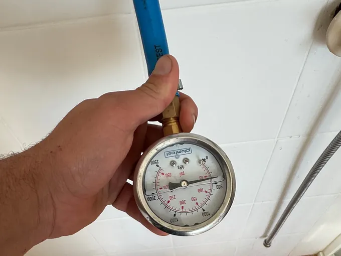 Plumber holding a pressure gauge connected to the shower pipework during a leak test in Prestons