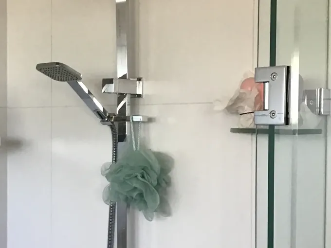 Hand shower on its rail in a tiled shower recess behind a glass screen in Merrylands