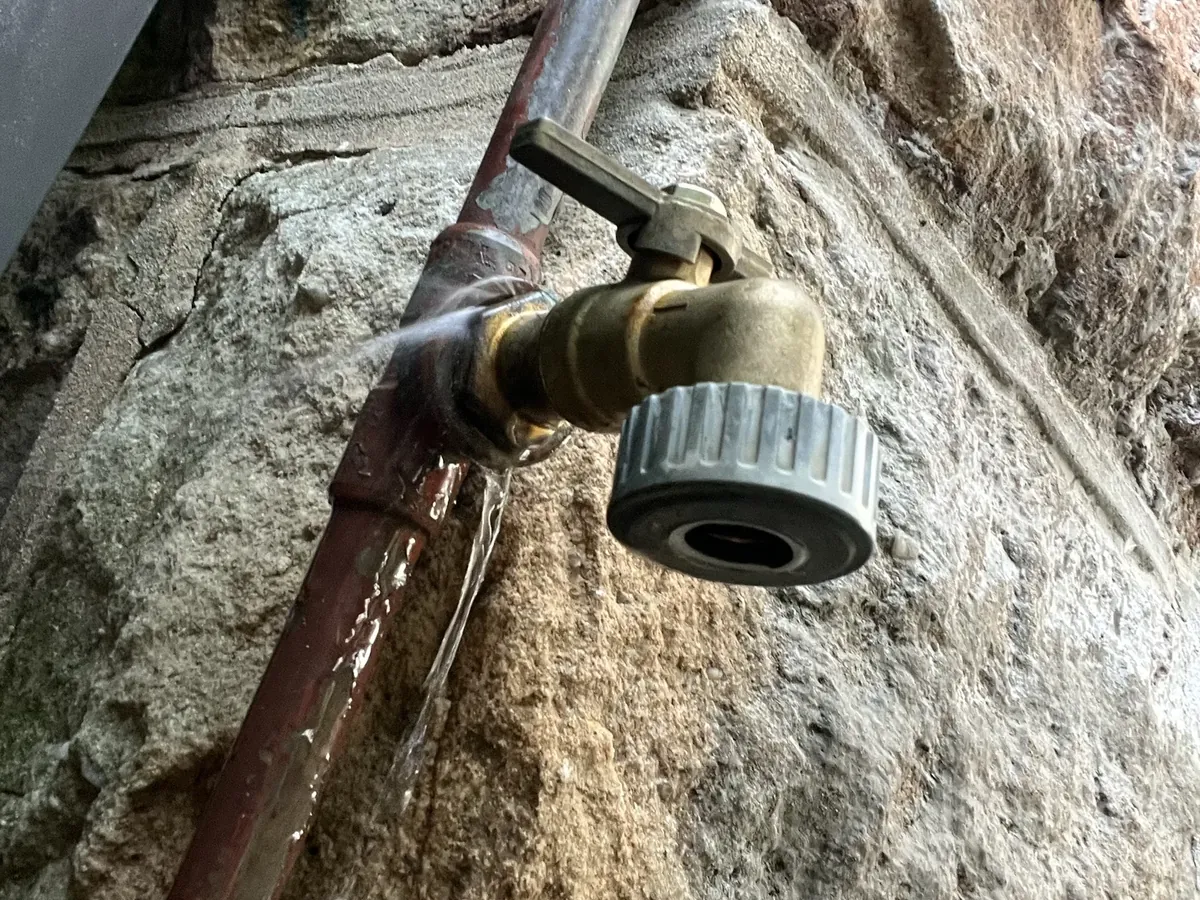 Water spraying from the joint behind a brass garden tap on a sandstone wall in Bondi Beach