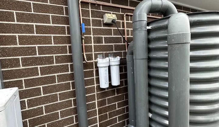 Twin water filter housings on new copper pipework beside a slimline rainwater tank in Marsden Park