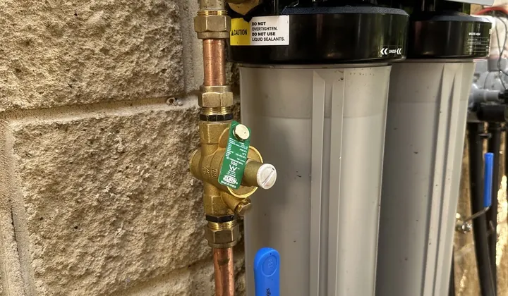 Filter housings with a pressure limiting valve and a blue-handled isolation valve on a tank water supply in Wilberforce