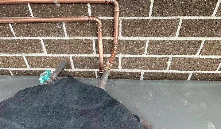 New copper pipework running up the wall from the outlet valves of a rainwater tank in Marsden Park
