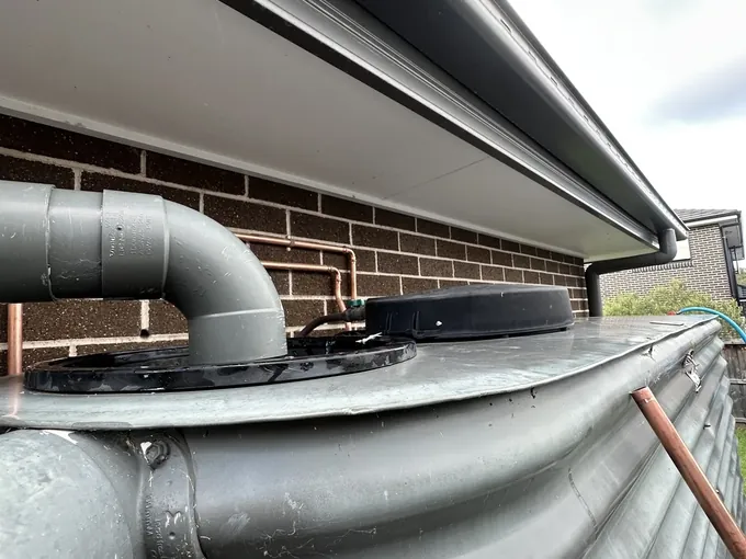 Copper water line on the wall above a slimline rainwater tank and its downpipe inlet in Marsden Park