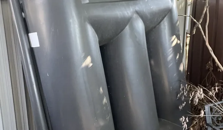 Slimline rainwater tank with its downpipe against a side fence in Mount Druitt