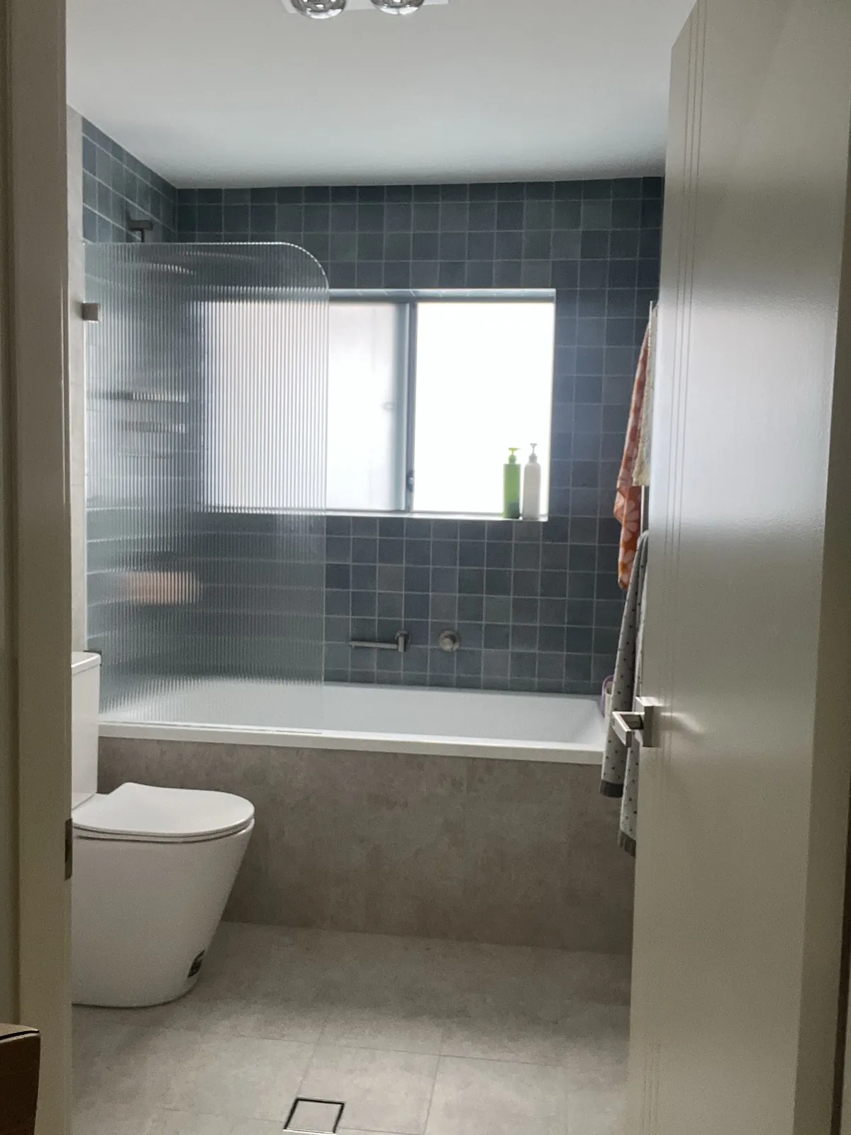 Renovation Plumber Sydney - a bathroom renovated end to end by Mr Splash in Padstow, with blue tiles, a bath with shower over and a heated towel rail