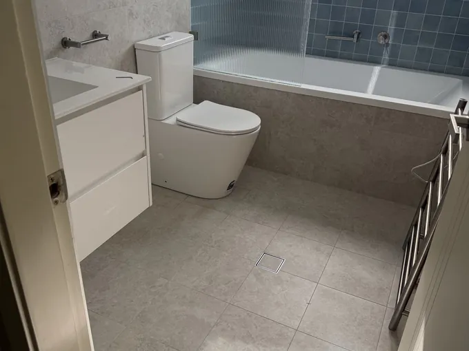 Renovated ensuite in Padstow seen from the doorway: wall-hung vanity, toilet, bath and heated towel rail