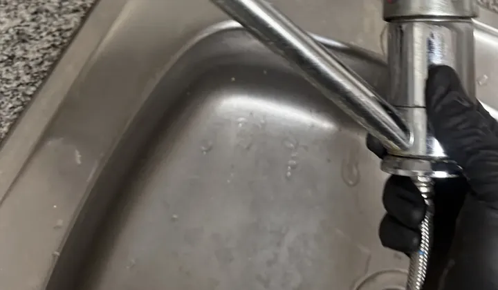 Plumber's gloved hand holding the pull-out hose of a kitchen mixer over a steel sink in Woolloomooloo