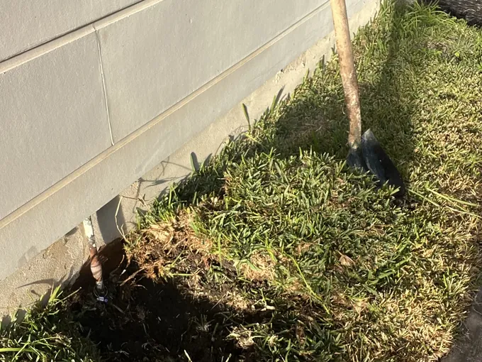 Spade in the lawn beside the turf lifted along the house wall to reach a leaking pipe in Roselands