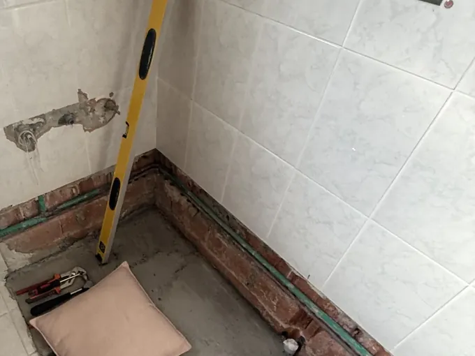 Bathroom floor opened up along the wall to reach the pipes, with a spirit level in Guildford