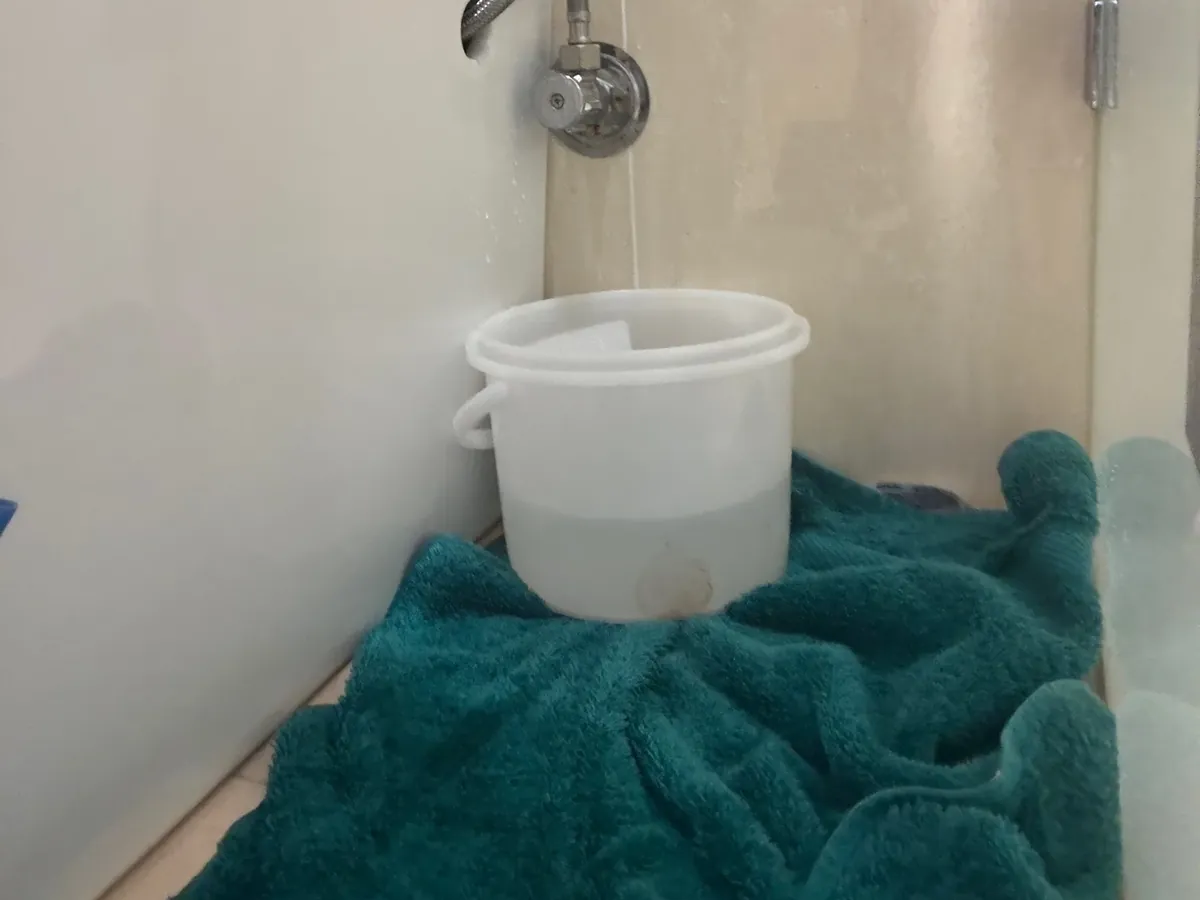 Bucket and towel catching water from a leaking toilet stop tap in a Newington bathroom