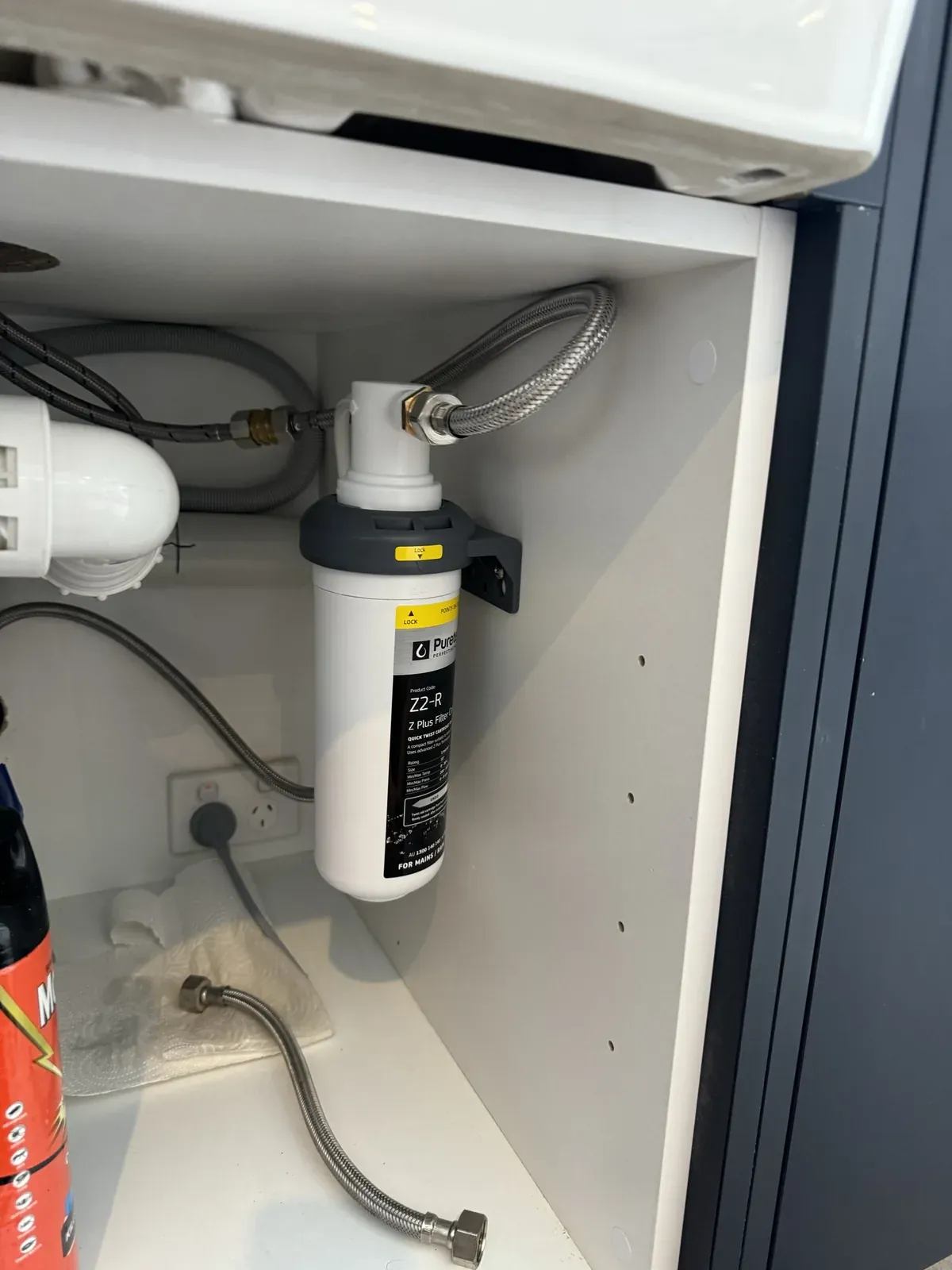 Customer-supplied twist-lock water filter on a bracket under a kitchen sink in Manly