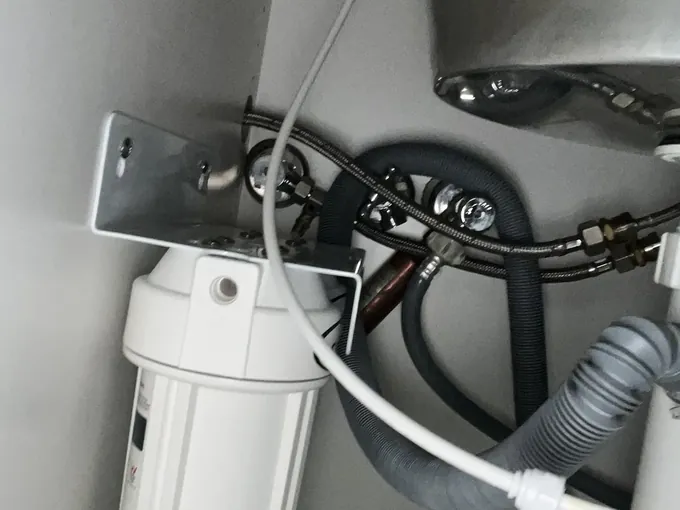 Isolation valves and braided hoses beside a bracket-mounted filter housing under a kitchen sink in Whalan