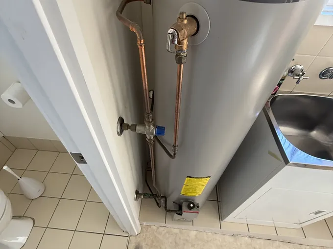 Rheem indoor gas storage hot water system in a laundry with its relief valve and copper pipework