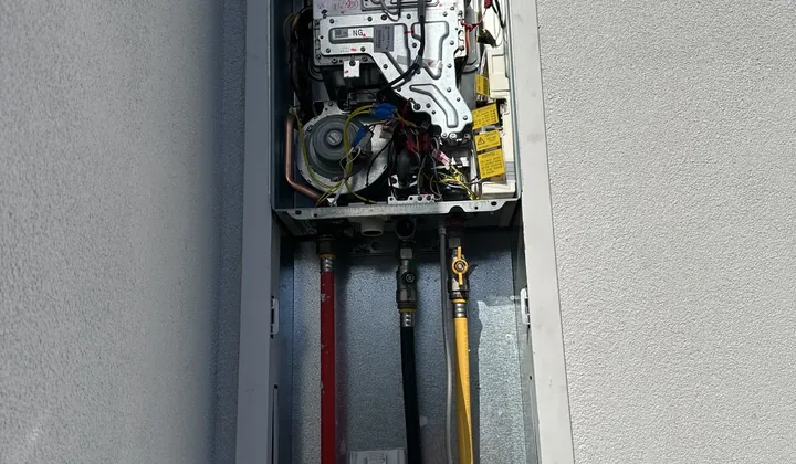 Gas continuous flow unit with its cover off in a recess box above red, black and yellow pipes in Spring Farm