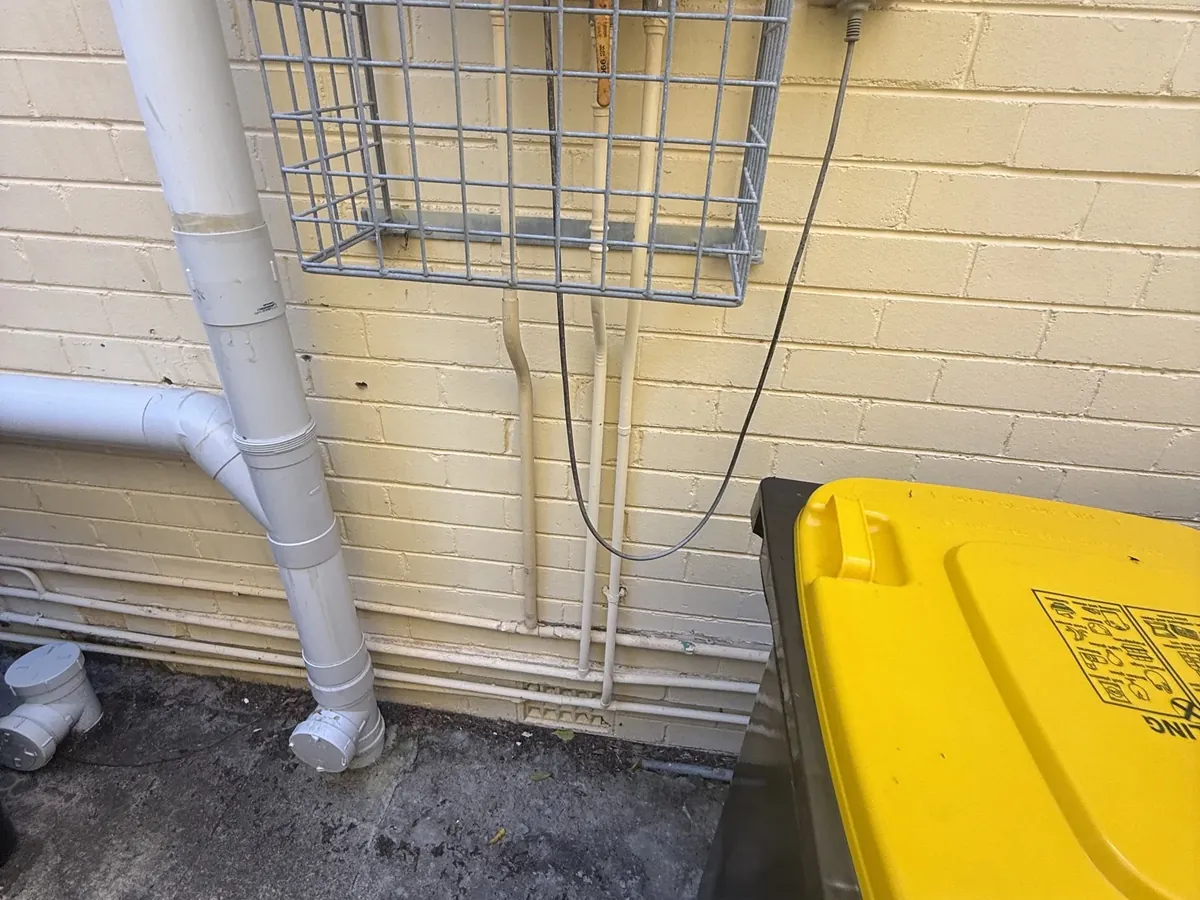 Old continuous flow gas unit behind a wire cage with its worn pipes below it in Oatley