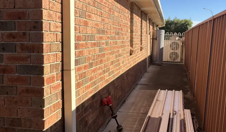 Downpipe down a brick corner beside new roofing sheets on a side path in Ingleburn