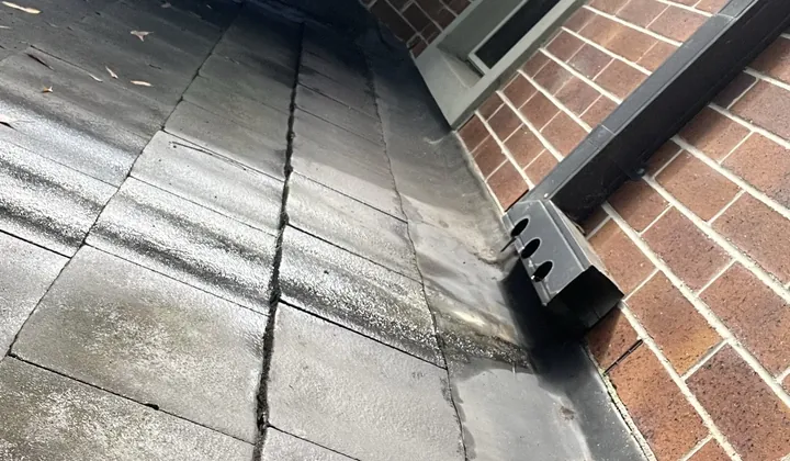 Tiled roof running along a brick wall under its flashing, with a downpipe spreader, in Wahroonga