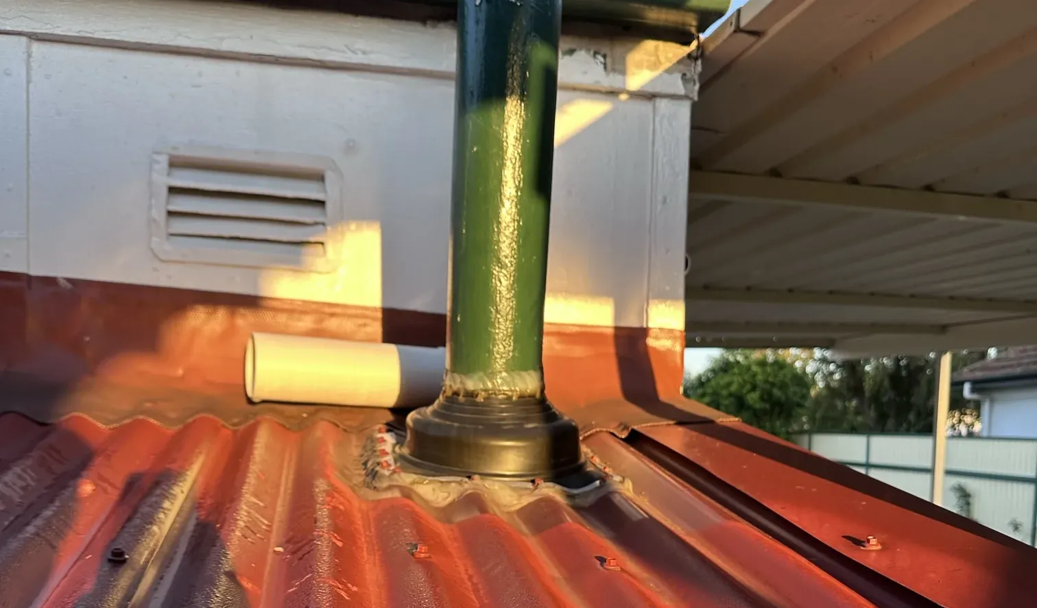 Green pipe sealed through a red corrugated iron roof with a rubber flashing boot in Greenacre