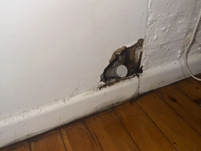 Hole opened in a wall at the skirting board to reach a leaking pipe
