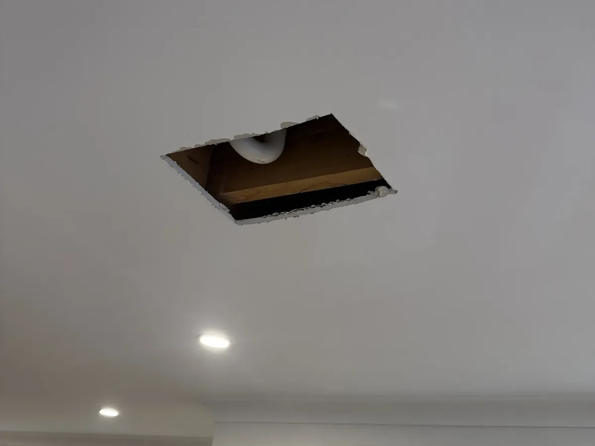 Square hole cut in a ceiling below a bathroom to reach a leaking pipe