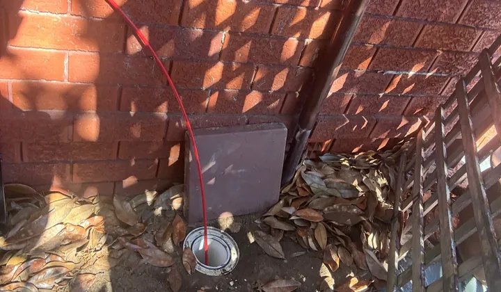 Jet blaster hose fed into an inspection opening in the corner of a yard in Beverly Hills