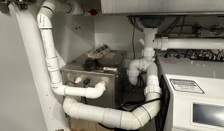Under-sink sullage pump and white waste pipes below a stainless sink at a workshop in Seven Hills