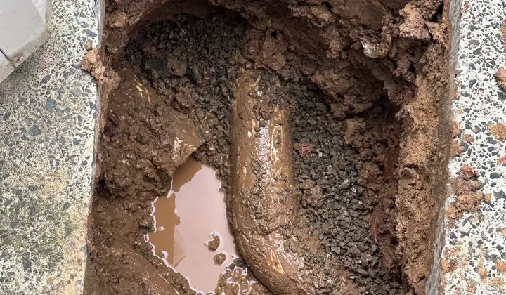 Trench dug through a concrete path to expose a buried drain pipe in Abbotsbury