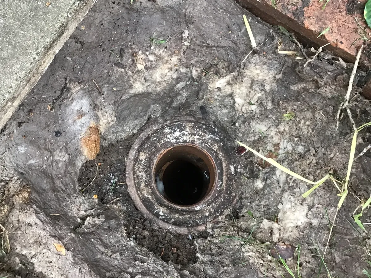 Old clay sewer inspection opening in the ground beside a path in Ermington