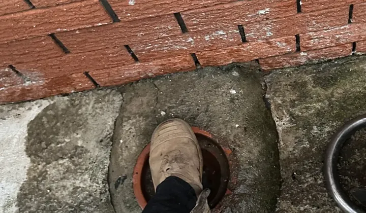 Plumber feeding a jetter hose into a terracotta sewer inspection opening at the base of a brick wall in Greystanes