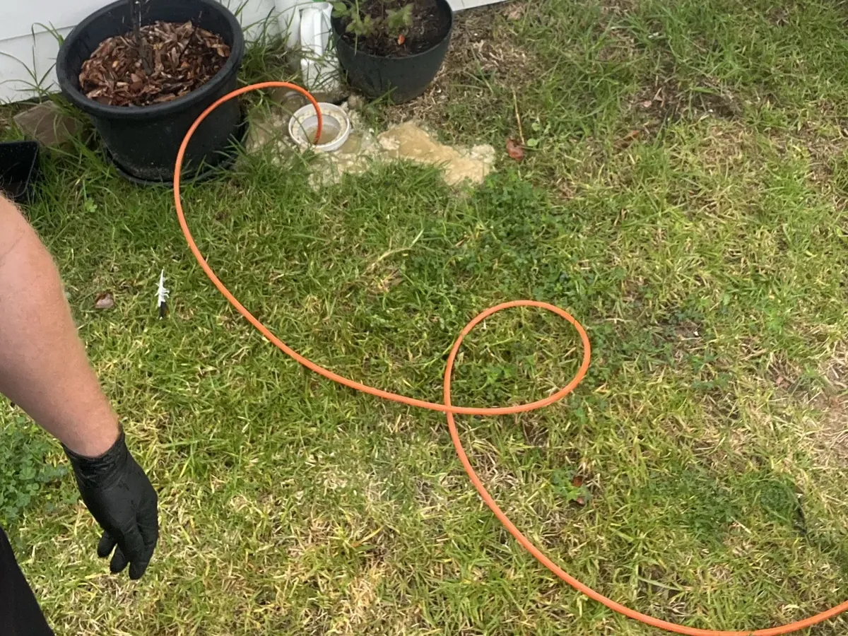 Jetter hose fed into an open sewer riser on a lawn, with grey sewage residue around it, in Campbelltown
