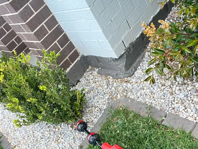 Red pipe locator on a lawn beside a gravel bed and a painted brick wall in Oran Park