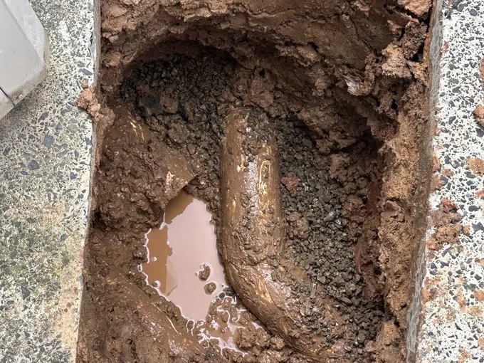 Hole saw-cut through a concrete path and dug down to a mud-covered drain pipe bend in Abbotsbury