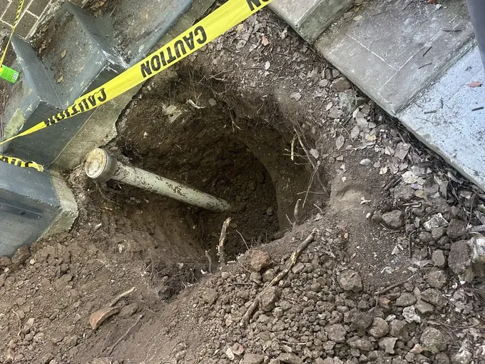 Deep hole dug beside a path with caution tape round it and a capped PVC pipe across it in Mount Druitt