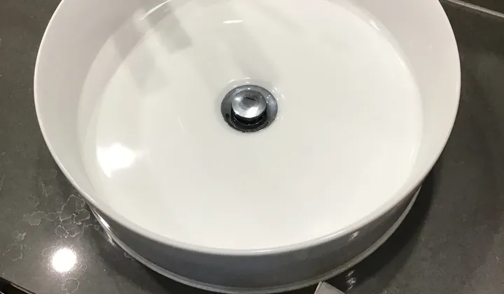 Round white vessel basin with a tall mixer on a dark stone bench