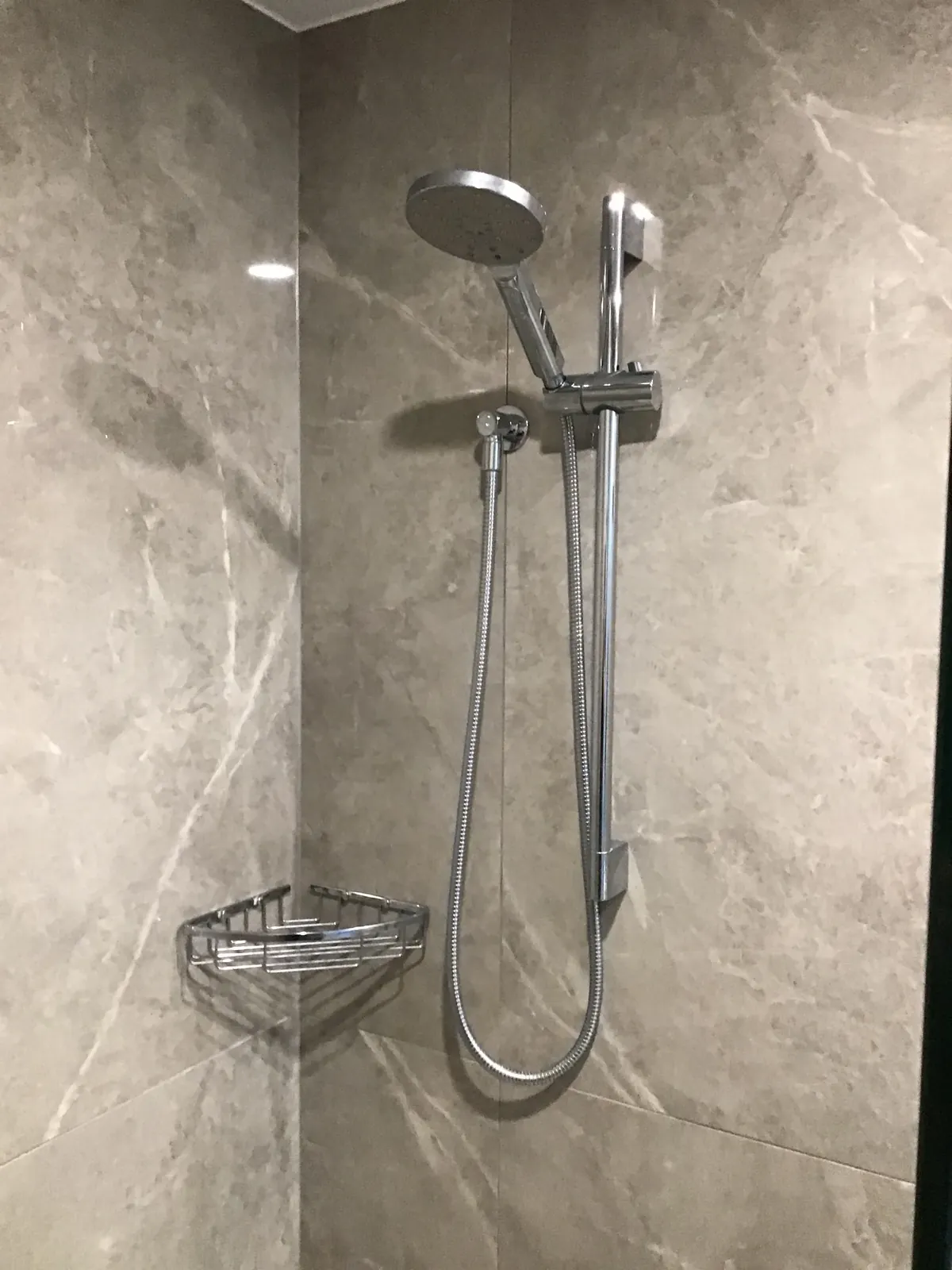 Rail shower with hand shower and corner basket in a large-format grey marble-look tiled shower