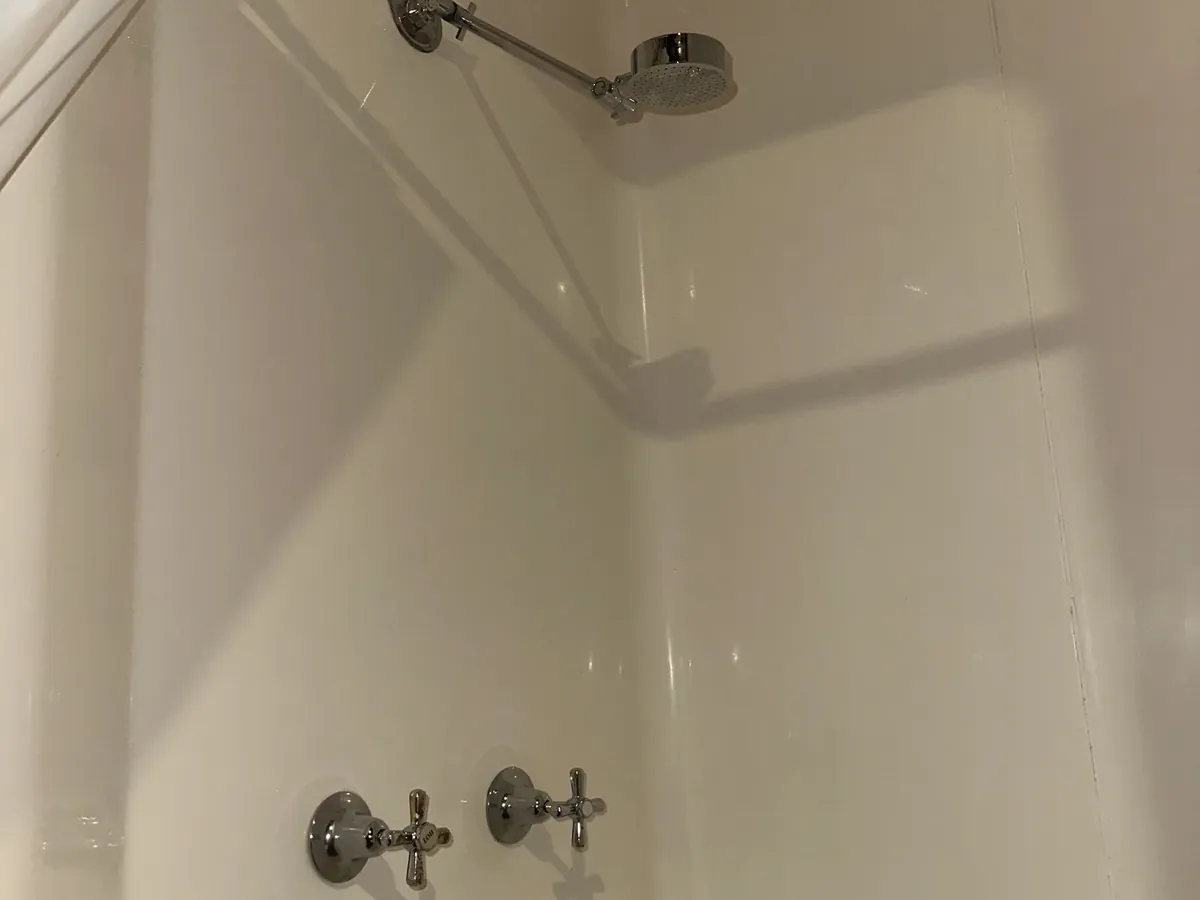Older shower with cross-handle taps and a fixed shower head